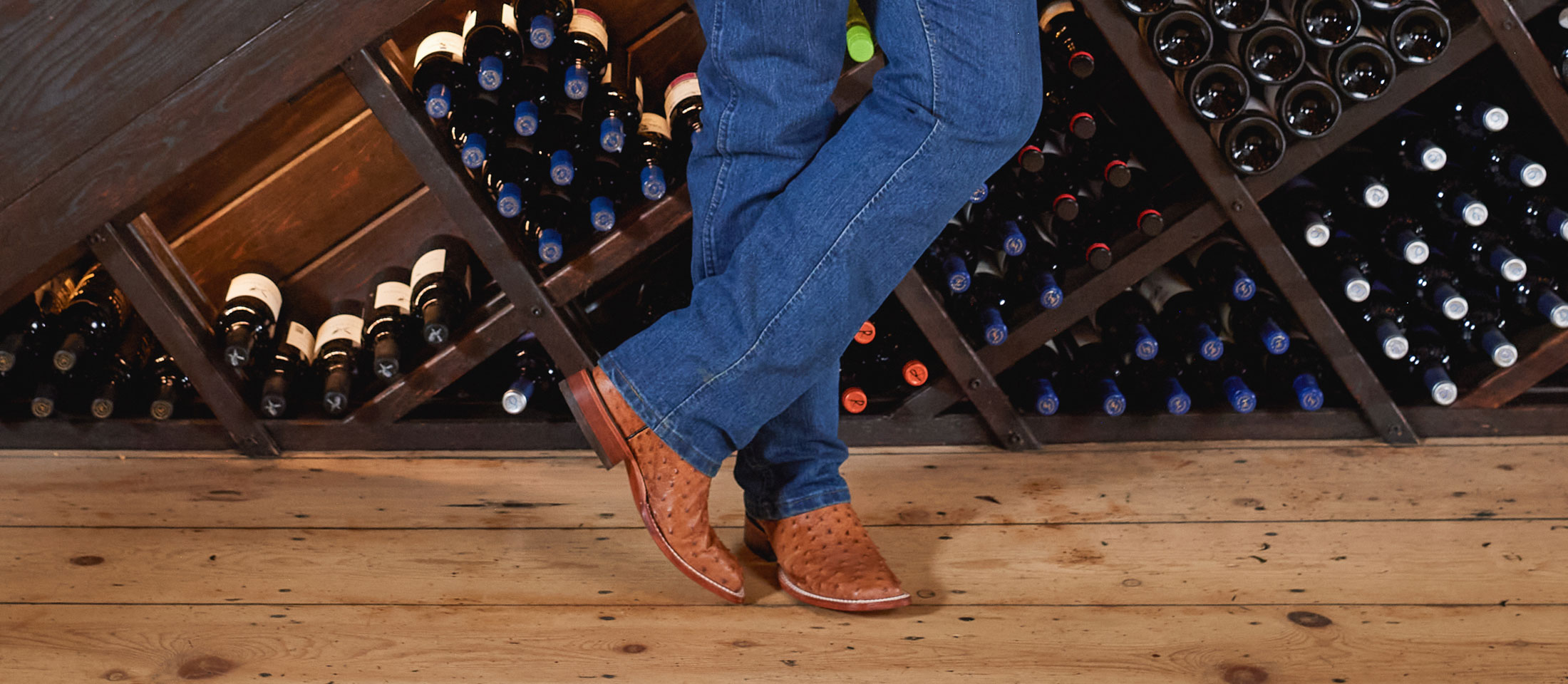Un hombre que lleva botas occidentales Justin está de pie frente a un estante de vinos.